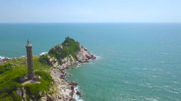 Vuurtoren op greenisland in blauwe zee luchtfoto landschap van drone vliegen. Vuurtoren op rotsachtige eiland in de Oceaan en blauw skyline achtergrond. — Stockvideo