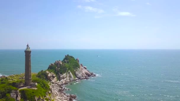 Vuurtoren op rotsachtig eiland in de blauwe zee luchtfoto landschap. Drone uitzicht vuurtoren op klif in Oceaan op blauwe achtergrond van water en lucht. — Stockvideo