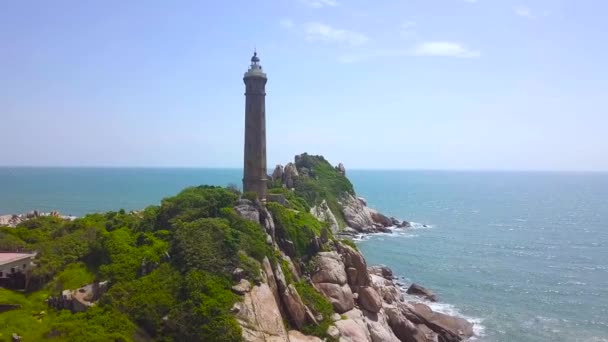 青い水の風景の空中で岩だらけの島の海光の家。ドローンに浮かぶ緑の島の灯台タワーを見る. — ストック動画