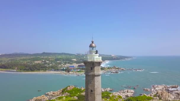 Sea light house on rocky island in blue sea and modern city on skyline deone view. Aerial landscape lighthouse tower on green island in ocean. — Stock Video