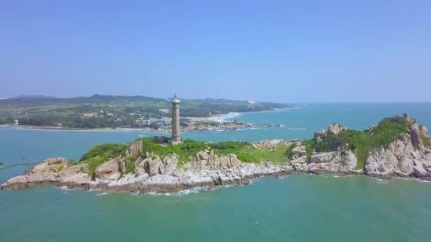 Sea Light hus på klippeøen i blåt hav og moderne by på skyline, panoramaudsigt fra drone. Luftudsigt fyrtårn på grøn ø i havet . – Stock-video
