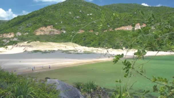 Mensen rusten op zanderige zomer strand en zwemmen in de turquoise zee op groene heuvel ladscape. Toeristische mensen op zee strand met kristalhelder water. Groene hooglanden op tropisch eiland. — Stockvideo