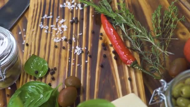 Закрыть овощи перец, помидор, лук, чеснок и травы розмарин, соль, оливки для приготовления пищи на кухне. Обстрел овощей и приправы на деревянном столе . — стоковое видео