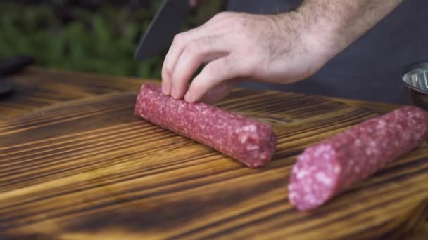 Närbild av kock kock med kniv för skärning korv pepperoni på skivor på träbord. Processen förberedelse ingrediens för italiensk pizza pepperoni på kök. Matlagning och mat förbereder koncept. — Stockvideo