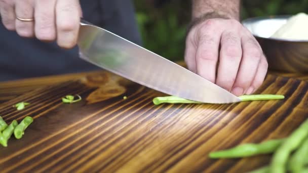 Cozinheiro Chef com faca de corte de feijão verde na mesa de madeira câmera lenta. Feche as mãos masculinas cortando feijão verde. Dieta vegetal e vegetariana. Conceito de cozinha de alimentos. Preparação de processo em cozinha . — Vídeo de Stock