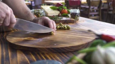 Şef yemek yeşil zeytin ahşap masa üzerinde bıçak ile kesme. Erkek Dilimleme zeytin Akdeniz salata için eller. Vejetaryen mutfağı için bitkisel madde. İtalyan restoranında yemek.