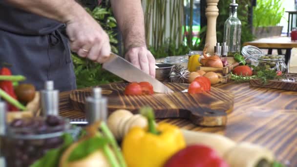 Cocinero de corte con cuchillo de tomate en el fondo de la composición de los alimentos. Hombre con cuchillo rebanando tomate fresco en la mesa de la cocina durante la preparación de alimentos. Cocinar platos vegetarianos. Nutrición y dieta saludables . — Vídeos de Stock