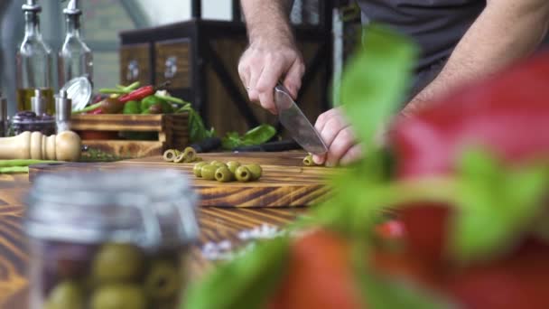 Hand cutting green olives with knife on kitchen table. Cook slicing olives for vegetarian salad. Vegatable ingredient healthy diet. Cooking food, process preparation concept. — Stock Video