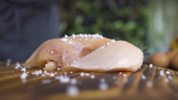 Black pepper pouring on raw chicken fillet on kitchen board close up. Fresh fresh chicken fillet marinating on wooden table. Seasoning meat for bbq. Cooking meat dish, food preparation concept. — Stock Video