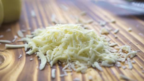Τριμμένο τυρί στο ξύλινο τραπέζι κοντινό πλάνο. Διαδικασία τρίψιμο γαλακτοκομικά τυριά σε τρίφτη στο πλοίο κουζίνα. Συστατικά για το μαγείρεμα πίτσα, σαλάτα, μακαρόνια, λαζάνια. Μεσογειακή, ιταλική και ελληνική κουζίνα. — Αρχείο Βίντεο