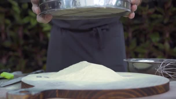 Chef sifting flour powder through sieve for baking slow motion. Male hand pouring flour on wooden board through sieve in bakery kitchen. Preparation ingredients for baking. Cooking food concept. — Stock Video