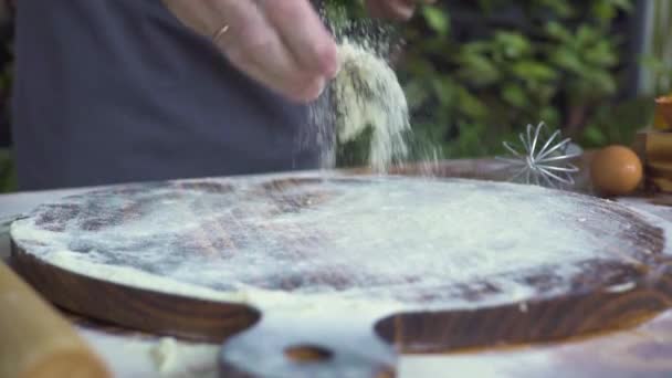 Пекарь наливает горсть муки на деревянную доску и месит тесто на деревянный стол. Шеф-повар готовит тесто для приготовления торта. Готовить макароны, пиццу, печь хлеб и пирог. Концепция приготовления пищи . — стоковое видео