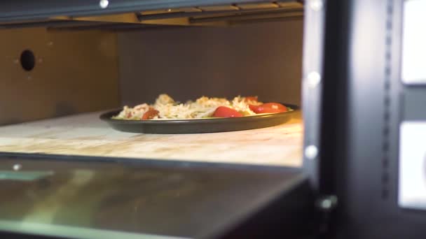 Pizza met kaas, tomaten en pepers bakken in hete kachel op Italiaans restaurant keuken. Traditionele pizza in moderne oven restaurant keuken koken. Voedsel bereiding concept, nationale gerechten. — Stockvideo