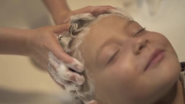 Detailní záběr tvář malého chlapce při mytí vlasy a hlavu v dětí kadeřnický salon. Kadeřník ruční mytí hlavy. Děti holičství salon. Kadeřník, mytí vlasů malého chlapce v holičství. — Stock video