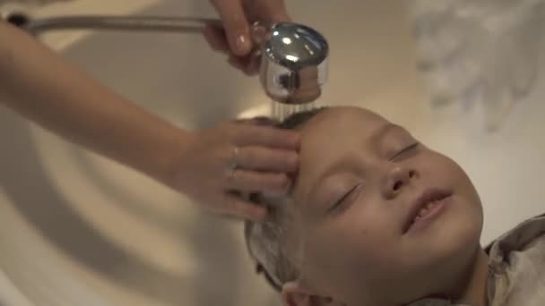 Kinderen Haarstylist wassen haar met shampoo te kleine jongen in Kapper salon. Close-up wassen kinderen hoofd in kapper. Mannelijke kapper wassen van hoofd naar het jongetje. Kid hair care concept. — Stockvideo