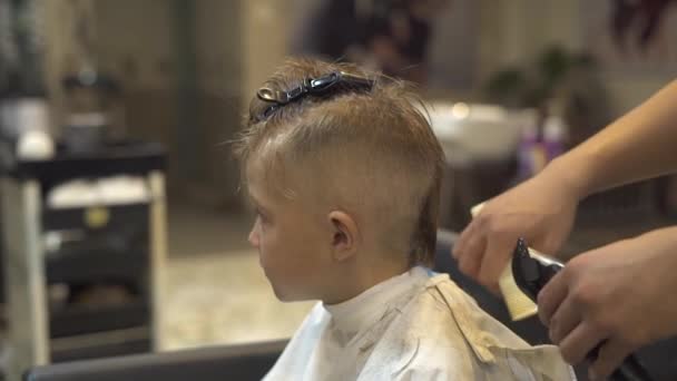 Cięcie włosów dzieci do małego chłopca z golarka elektryczna w fryzjer salon fryzjerski. Dzieci fryzura z włosów maszyny z bliska. Fryzjer robi dziecko fryzurę w dzieci salon fryzjerski. — Wideo stockowe