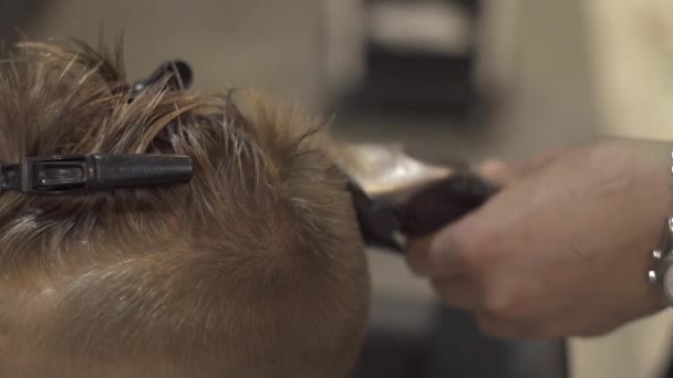 Crianças cabeleireiro cortando menino com lâmina elétrica no salão de cabeleireiro. Haidresser fazendo penteado miúdo com barbeador elétrico em crianças barbearia close up. Menino conceito de corte de cabelo . — Vídeo de Stock