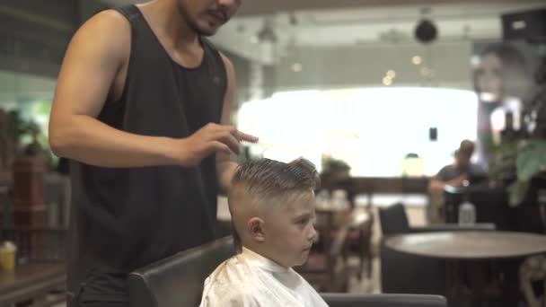 Fryzjerka cięcia małego chłopca z włosów maszyny w fryzjera. Bliska strzyżenie chłopca w salon fryzjerski. Chłopiec fryzurę grzebień i golarka elektryczna. Fryzjer Robienie dzieci fryzurę. — Wideo stockowe