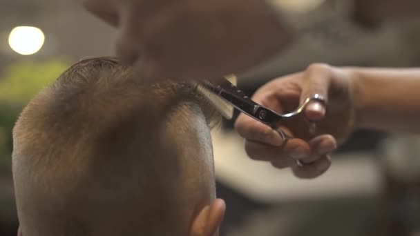 Peluquero corte el cabello con tijeras de peluquero y peine en peluquería de cerca. Niños corte de pelo con tijeras de pelo. Peinado de niño en peluquería. concepto de corte de pelo niño . — Vídeos de Stock