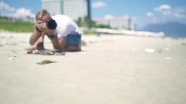 Erkek fotoğrafçı fotoğrafçılık genç kadının kumsalda poz alarak. Genç fotoğrafçı profesyonel modeli ile yaz plaj üzerinde çalışan adam. Fotoğraf makinesi fotoğraf oturumu için kullanan adam.