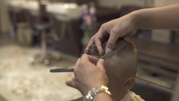 Barbier utilisant rasoir droit pour le rasage des cheveux sur la tête du petit garçon dans le salon de coiffure. Gros plan rasage cheveux avec rasoir rétro dans le salon de coiffure. Enfants coupe et garçon coiffure . — Video