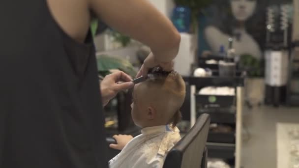 Concepto de peinado infantil. Peluquería con afeitadora en salón masculino. Peluquero usando navaja de afeitar para afeitar al niño. Peluquería haciendo peinado chico en salón de peluquería . — Vídeo de stock