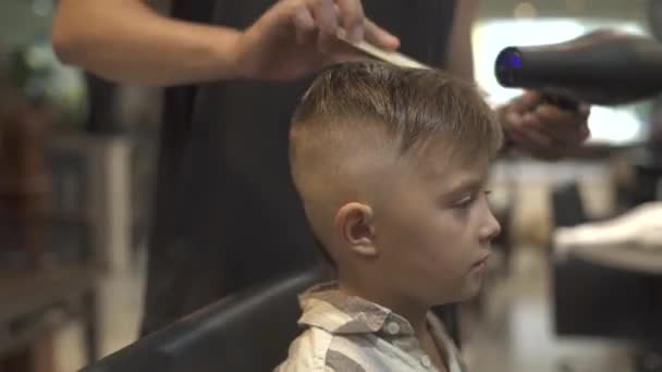 Мальчик прическа с сушилкой в парикмахерской. Детская сушка волос в парикмахерской. Парикмахер укладки волос маленький мальчик с сушилкой. Закончи парикмахерскую. Детская прическа . — стоковое видео