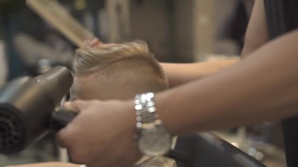 Cabeleireiro fazendo penteado menino com secador na barbearia. Crianças secagem de cabelo no salão de cabeleireiro. Cabeleireiro styling cabelo menino com secador. Terminar cabeleireiro crianças penteado na barbearia — Vídeo de Stock