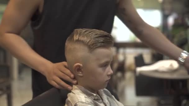男孩发型的概念。理发师在理发店做儿童发型。理发师在理发店里创造男孩发型。男沙龙里的小男孩。儿童发型概念. — 图库视频影像
