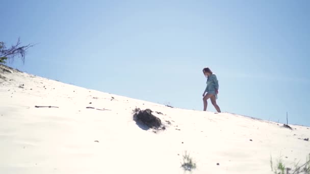 Jonge vrouw lopen op zandige duin in de hete woestijn op blauwe hemelachtergrond. Mooi meisje lopen op zanderige heuvel tijdens het reizen in de zomer woestijn. — Stockvideo