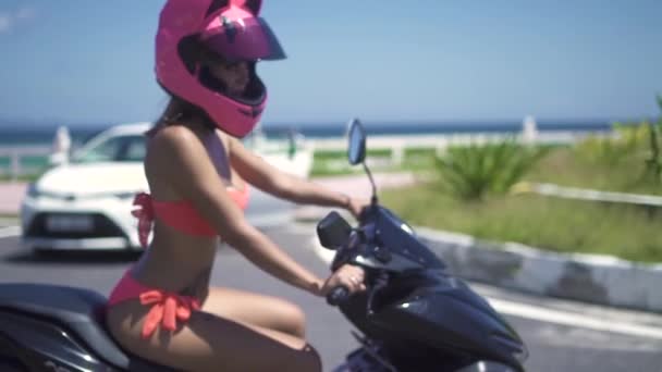 Moto piękna kobieta w różowe bikini i hełm jazdy na motocykl na morze plaża krajobraz zwolnionym tempie. Piękna kobieta w bikini i kask na motor bike. — Wideo stockowe