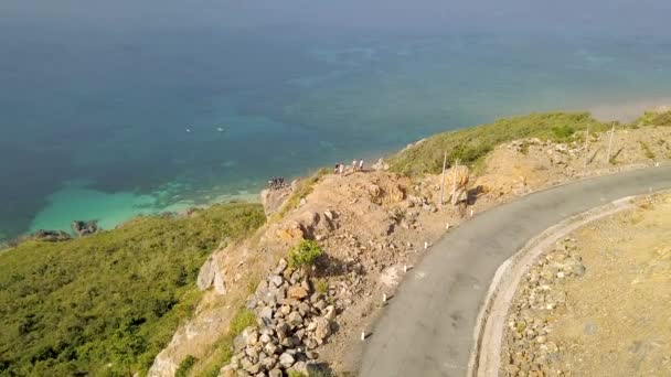 Turist människor på cliff edge med vacker utsikt på blå havet. Flygfoto resenärer på toppen av berget på shore turkosa havet och slingrande väg. Drone Visa blå havet landskap från berg. — Stockvideo