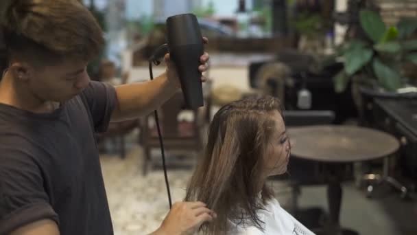 Man Frisör torkning håret av ung kvinna efter tvätt i frisörsalongen. Frisören använder hårtork för kvinnlig frisyr och skärning i barbershop. Kvinna frisyr och skönhet. — Stockvideo