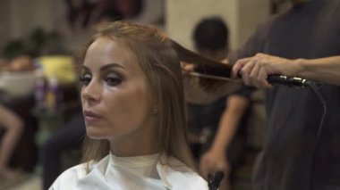 Güzellik Salonu saç düzleştirme sırasında genç bir kadın. Kuaför saç demir ve tarak için kadın saç şekillendirme kuaförlük Studio kullanarak. Kuaför kadın saç modeli maşa ve tarak ile oluşturma.
