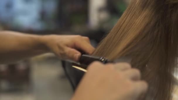 Barber using hair iron for straightening hair while hairstyling in hairdressing salon. Close up female hairstyling in professional studio. Hairstylist creating woman hairstyle in barbershop. — Stock Video