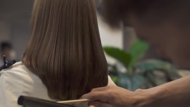 Hairtylist česání dlouhých vlasů, kadeřnictví v kadeřnictví. Žena kadeřnictví s žehlička na vlasy pro rovnání v kosmetické studio. Master vytváření ženský účes v holičství. — Stock video