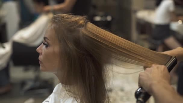 Cabelo alisamento estilista com pinças quentes no salão de cabeleireiro. Close up penteado feminino com ferro de cabelo no salão de beleza. Mestre criando penteado feminino na barbearia . — Vídeo de Stock