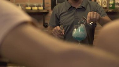 Barmen alkollü kokteyl bar sayacı, mavi içki ve buz ile kafede yapma. Buz yaparken cam masa bar kokteyl içki dökülen barmen.