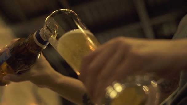 Hands pouring beer from bottle in glass in pub bar, restaurant or cafe close up. Waiter hands pouring bottle beer in glass in pub. Slow motion, low angle view — Stock Video