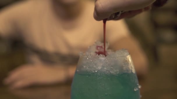 Barman vertiendo licor rojo sobre hielo mientras prepara cócteles alcohólicos en el mostrador del bar en el pub. Primer camarero haciendo cóctel con hielo y licor de color en vidrio en la mesa del bar en el restaurante . — Vídeos de Stock