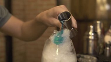 Gece kulübünde alkollü kokteyl bar counter yaparken buz üzerinde mavi içki dökülen barmen. Barmen buz ve mavi içki int cam akşam Restoran tabloda bar kokteyl yapmak.