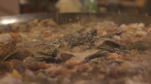 Gieten van rijst voor zeevruchten paella bereiden met mosselen, garnalen in hete pan close-up. Proces voorbereiding Spaanse paella in restaurant keuken. Kook preparating rijst met zeevruchten. Voedsel achtergrond. — Stockvideo