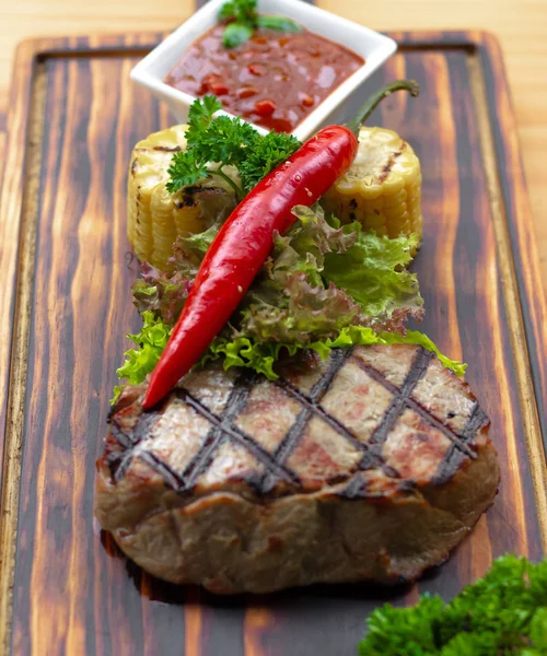 Composición del filete de carne barbacoa. Filete a la parrilla con pimiento rojo picante, hierbas, maíz y salsa de tomate sobre tabla de madera. Fondo de alimentos en el espacio de copia de madera. Nutrición saludable y concepto de dieta . —  Fotos de Stock