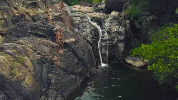 Pessoas pulando e nadando na cachoeira da montanha na vista aérea da floresta tropical. Pessoas mergulhando na água do rio que flui da cachoeira da montanha na floresta tropical . — Vídeo de Stock