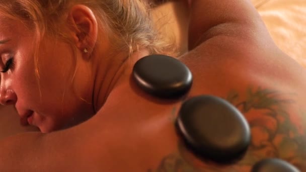 Giovane donna rilassante nel salone termale con massaggio corpo in pietra calda. Trattamento lapideo e massoterapia. Concetto zen e relax. Cura del corpo e della pelle nel salone spa . — Video Stock