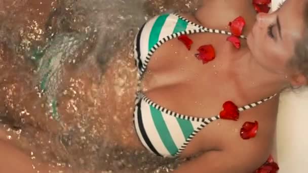 Donna in bikini che fa il bagno jacuzzi con petali di rosa nella spa. Bella ragazza sdraiata nella vasca idromassaggio nel resort termale di lusso. Terapia di bellezza e cura del corpo concetto . — Video Stock