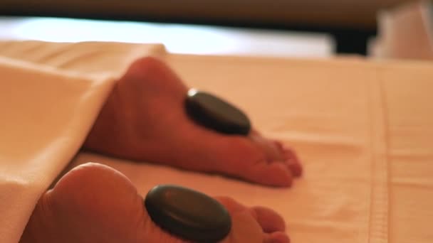 Masaje de pies con piedra caliente y terapia de spa en un hotel resort de lujo. Mujer joven relajante mientras que el masaje de piedra en el salón de spa. Relajación corporal y cuidado de la piel. Estilo de vida saludable. Concepto de bienestar — Vídeos de Stock