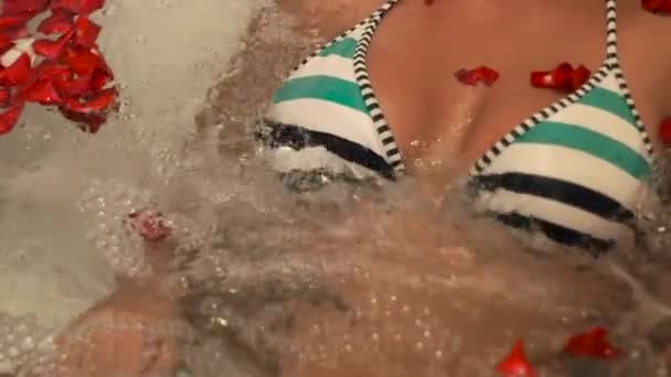 Frau im Bikini beim Whirlpool-Bad mit Rosenblättern im Wellnessbereich. Nahaufnahme sexy Mädchen in der Whirlpool-Badewanne im Luxus-Wellness-Resort liegen. Schönheitstherapie und Körperpflegekonzept. — Stockvideo
