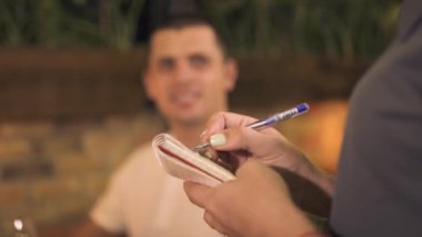 Genç adam gıdalardan sipariş alarak ve not defteri akşam restoranda garson kapatın. Romantik kafede yemek siparişi. Romantik restoranda garson servis Konuk.