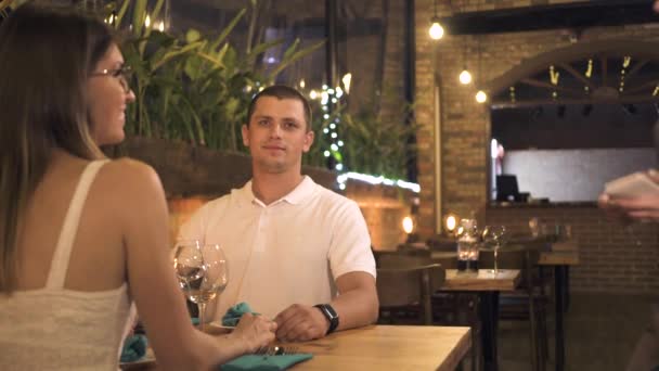 Romantický pár sedí u jídelního stolu v restauraci večer. Muž a žena mluvila s servírka při romantické večeři v elegantní restauraci. Pár v milování pořadí v kavárně. — Stock video